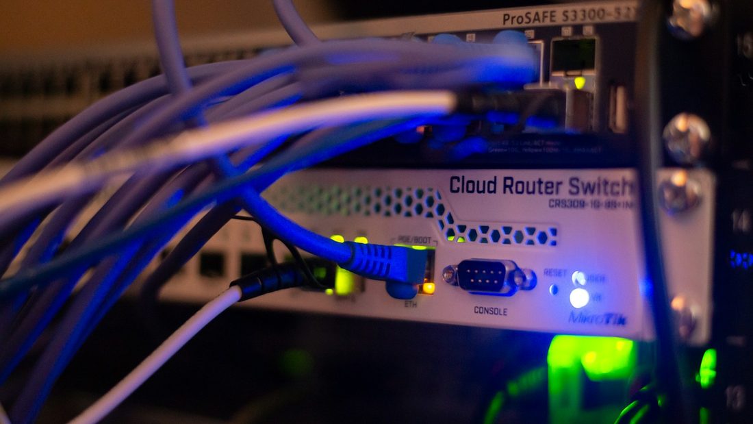 A MikroTik Cloud Router Switch in a rack with blue network cables plugged in and status LEDs lit