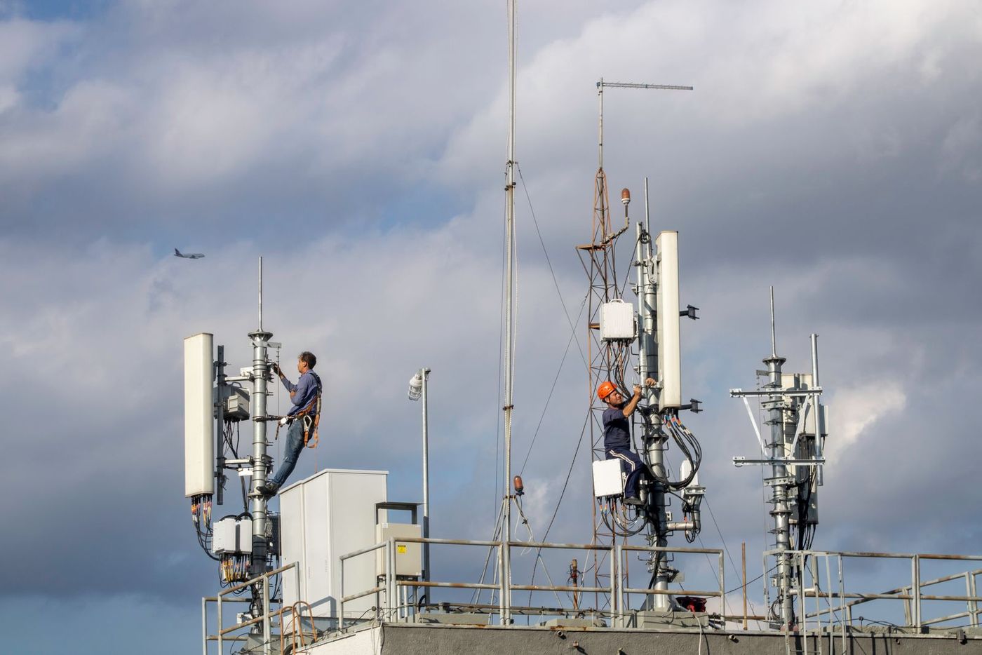 Technicians working on rooftop antenna masts under a cloudy sky
